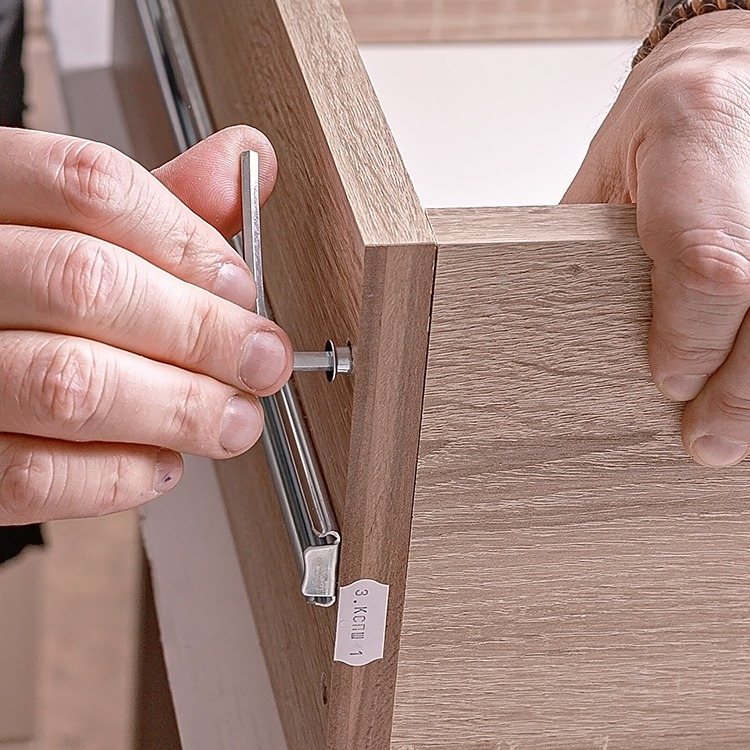 Hands driving a Hapric threaded insert into the edge of a wooden furniture panel